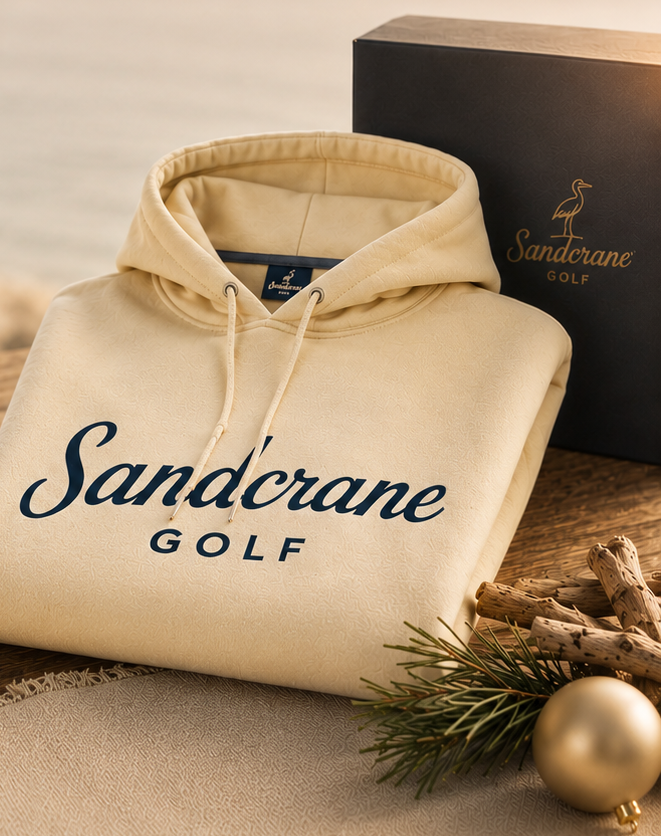 Beige hoodie with 'Sandcrane Golf' logo on a wooden surface with a scenic background